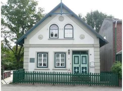 Das weiße Gorch-Fock-Haus mit grünen Türen und Gartenzaun am Nessdeich